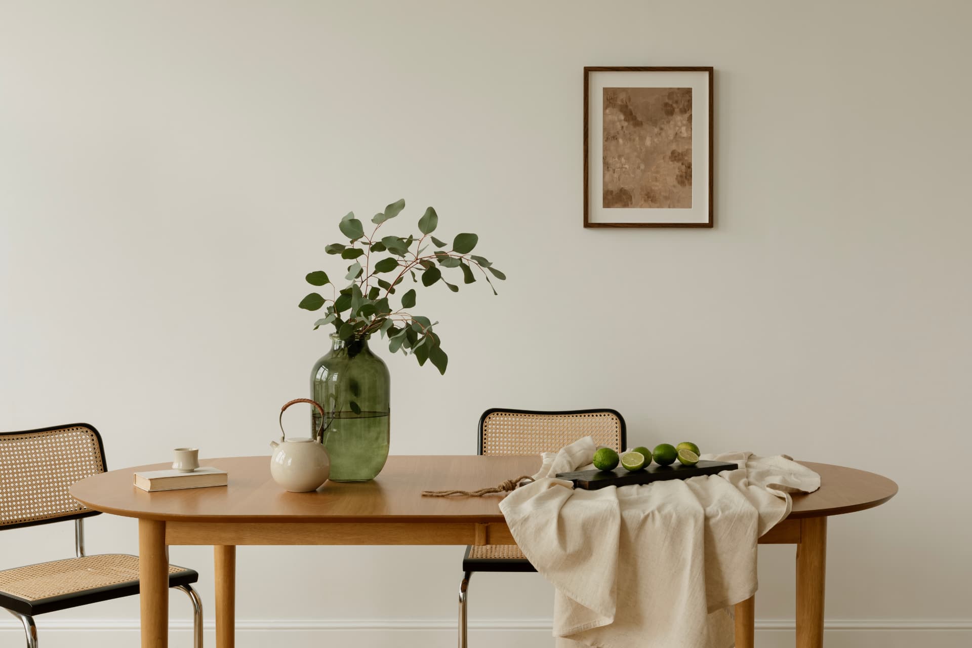 Dining area with a timber table, woven chairs, greenery and framed artwork